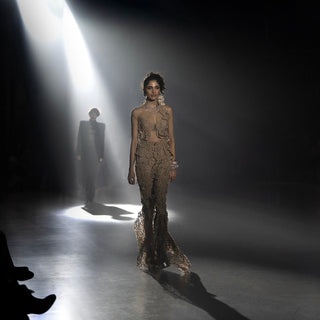 Woman’s intricate taupe couture evening gown on runway with spotlight highlighting lace detailing