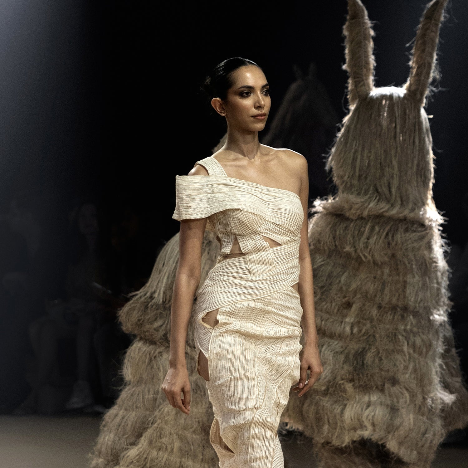 Close-up of model in asymmetrical cream textured dress with cutout detailing – modern resort fashion on runway