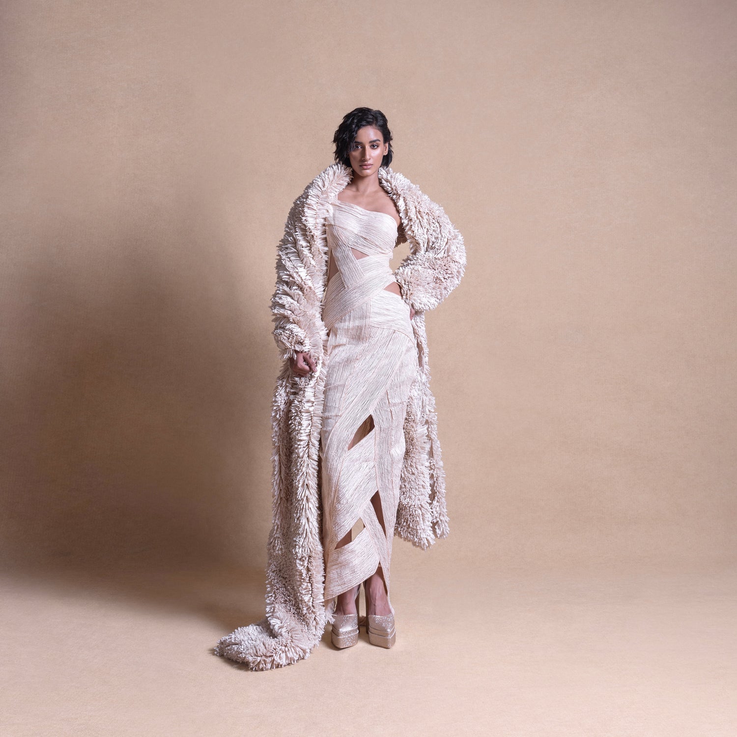 Model in textured coat and cut-out cream dress – full-length fashion editorial pose, creative fashion design, fitted dress, resort wear