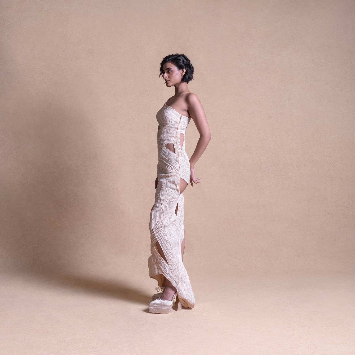 Model in cream sculptural cut-out dress – side profile showcasing asymmetric design