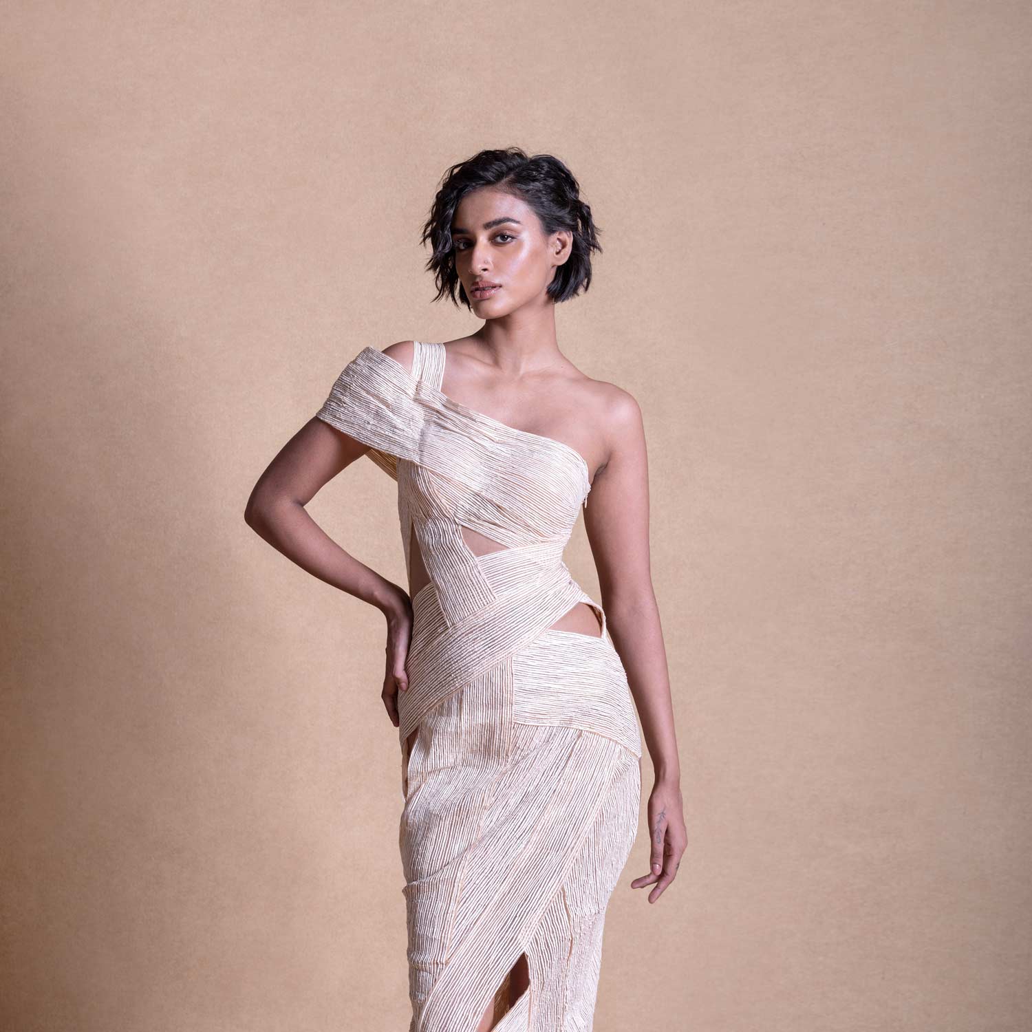 Studio portrait of model in asymmetric cream dress with wrap-style cutouts – contemporary resort fashion