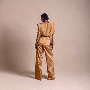 Back view of a model wearing a Structured designer jacket and flared pants, standing against a beige backdrop - high fashion ensemble, powershoulder jacket, metallic.