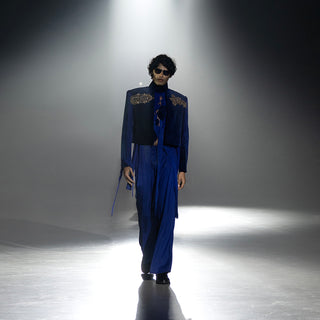 Men’s royal blue embroidered jacket with wide-leg trousers walking runway under dramatic spotlight