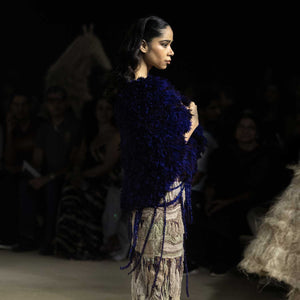Side profile of model in navy textured cape and ruched earthy-toned skirt with beaded fringe – modern artisanal runway style, high fashion couture look, navy blue textured cape
