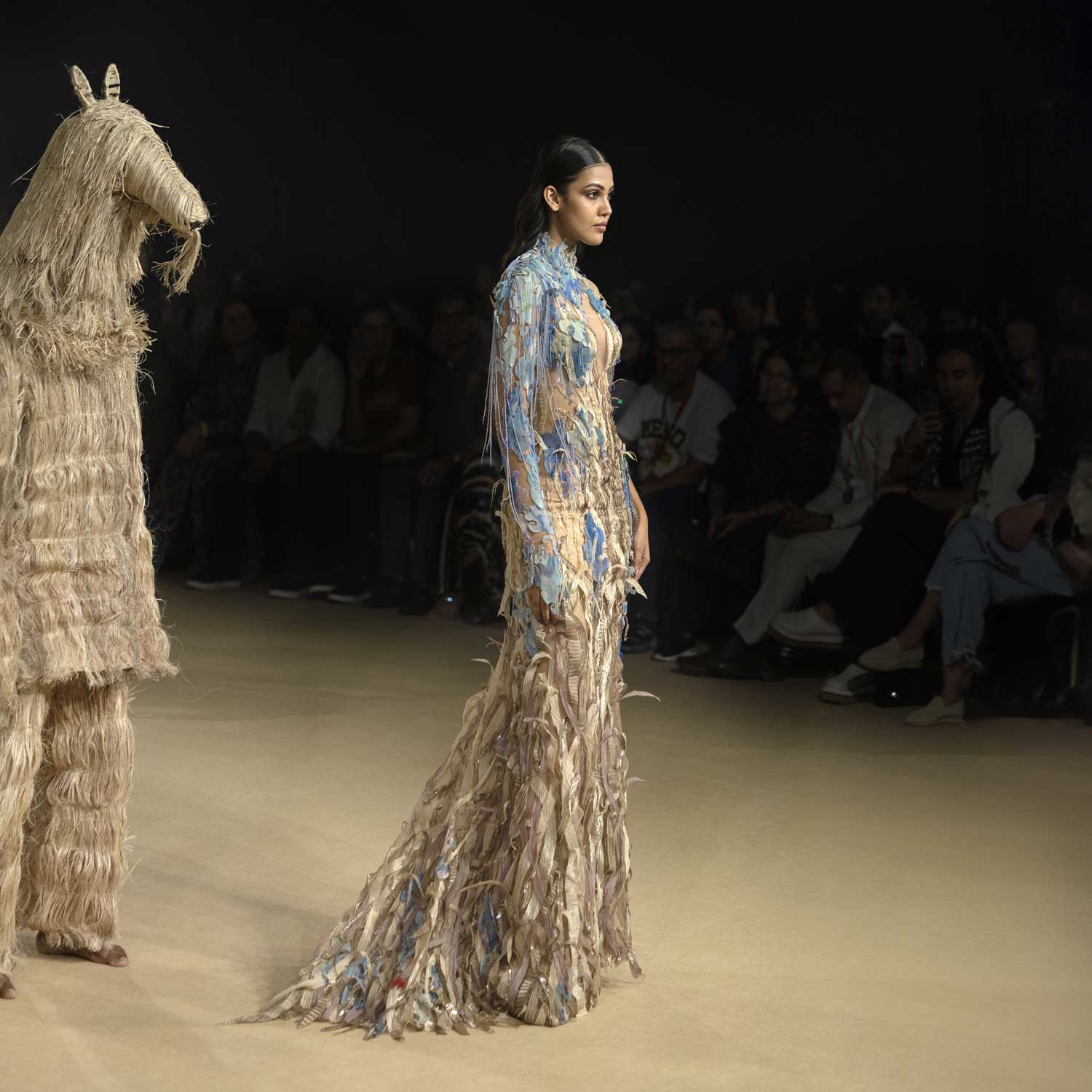 Model in earth-toned and blue sustainable gown with shredded textures on runway - eco-luxury fashion, reception gown