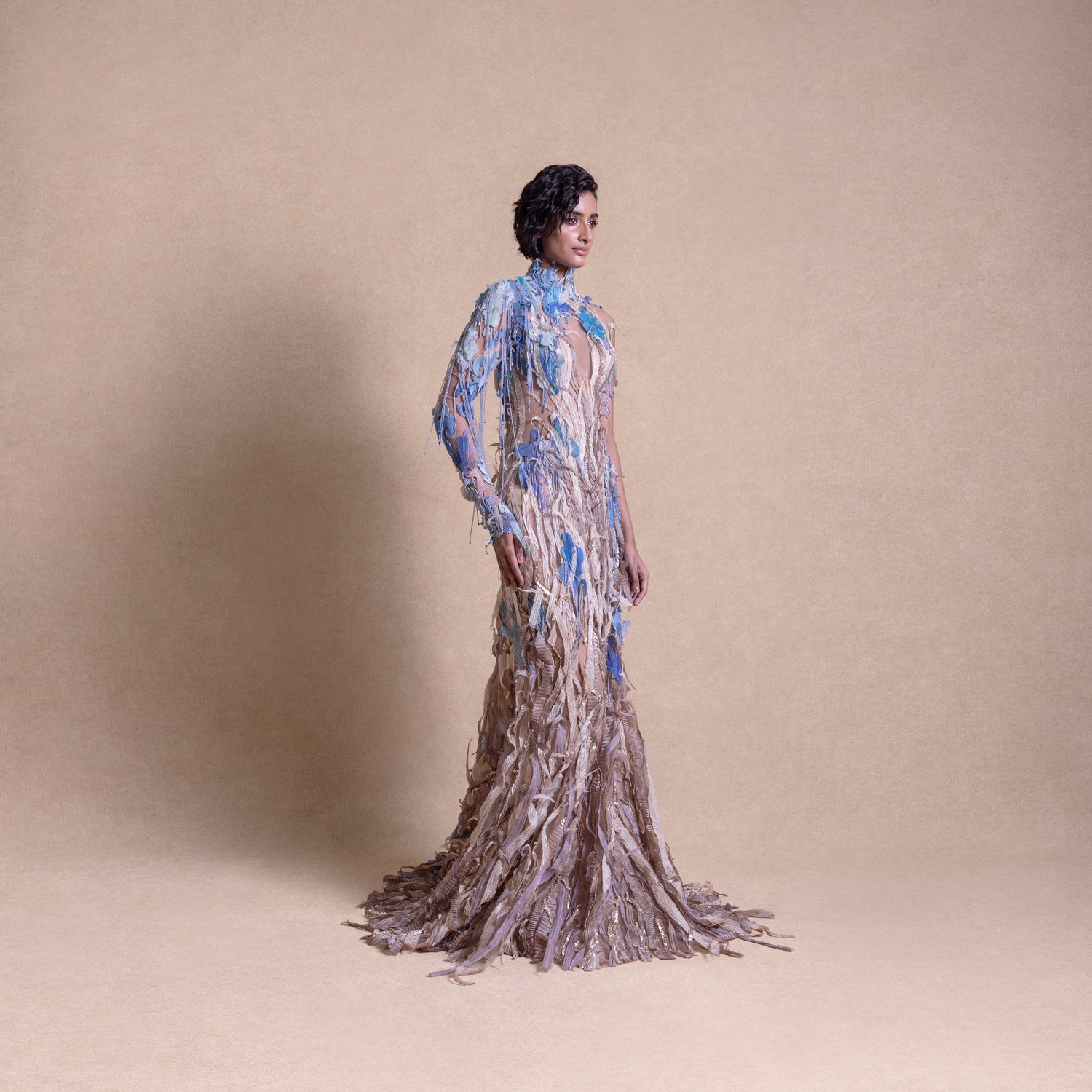 Side view of model in flowing earth-toned gown with blue floral embroidery and textured embellishments - eco-luxury fashion, reception gown, sustainable runway look