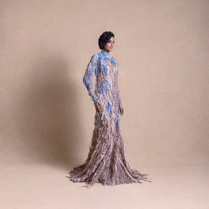 Side view of model in flowing earth-toned gown with blue floral embroidery and textured embellishments - eco-luxury fashion, reception gown, sustainable runway look