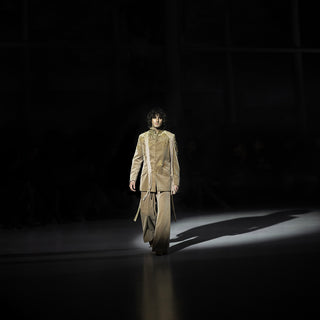 Men’s beige embellished bandhgala jacket with matching trousers walking runway under dramatic spotlight