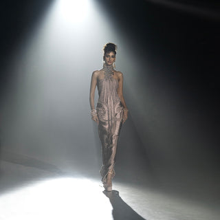 Women’s metallic fitted evening gown with ornate detailing walking runway under dramatic spotlight at fashion show
