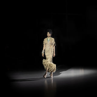 Women’s metallic gold cape and tiered ruffle skirt ensemble walking runway under dramatic lighting