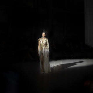 Women’s ivory embellished draped gown with metallic detailing and high slit walking runway under spotlight