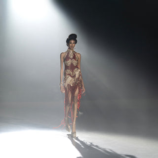 Women’s red fringe evening dress with gold embroidery walking runway in spotlight highlighting high-fashion detailing