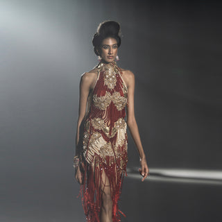 Model wearing a glamorous red and gold dress with fringe details on a dark background