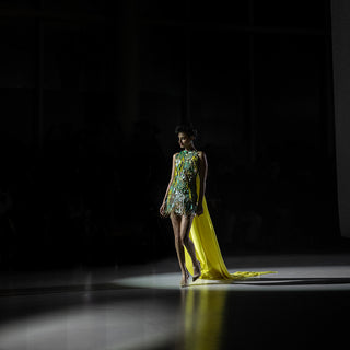 Women’s embellished short dress with multicolor embroidery and yellow sheer train walking runway under spotlight
