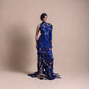 Model poses in a detailed electric blue sheer gown with textured appliqué, one-sleeve design, and high neckline - red carpet couture gown, cocktail gown