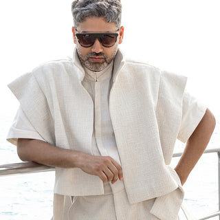 Men's ivory structured jacket layered over fluted half-sleeve shirt and wide-leg trousers – modern monochrome ensemble 