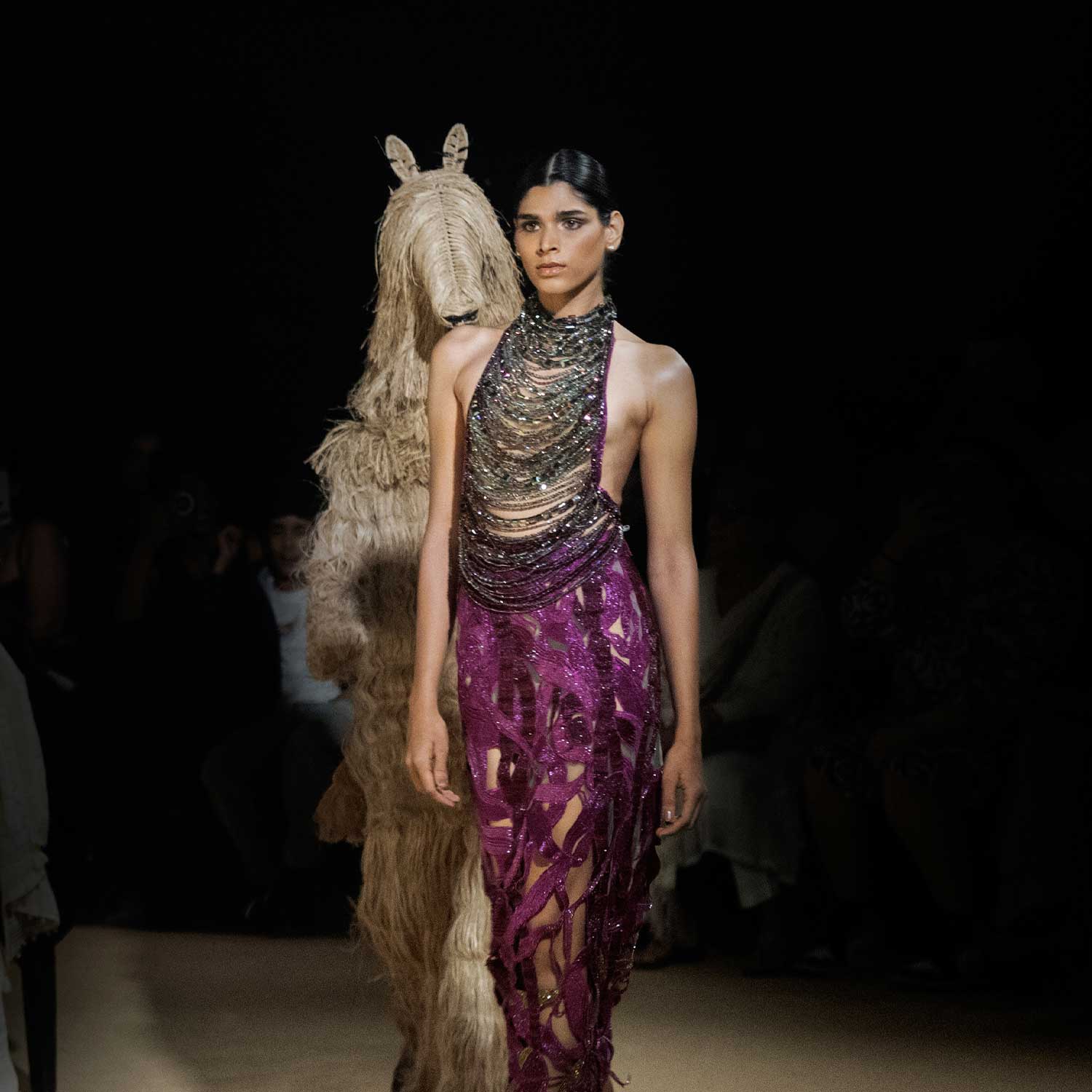Runway model in metallic chain-embellished halter top and purple sheer skirt, avant-garde fashion statement - purple embellished skirt, metallic chain top, bold designer outfit