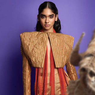 Female model in structured metallic gold cropped jacket with flared pants, posing against a purple backdrop - high fashion ensemble, powershoulder jacket, metallic.