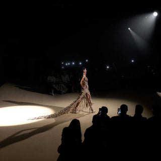 Runway model in nude embellished corset gown with dramatic train under spotlight -  couture runway dress, spotlight gown,