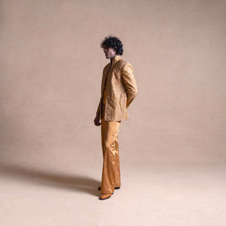 Model in gold textured Bandhgala suit with structured shoulders and matching trousers , standing sideways against a beige studio background - Tuxedo, retro suit, menswear