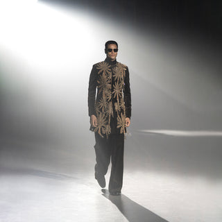 Men’s black velvet embellished short sherwani with gold embroidery walking runway under spotlight