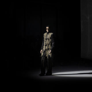 Men’s black velvet short sherwani with intricate gold leaf embroidery and tailored trousers on runway