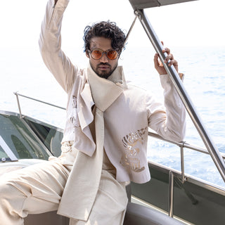 Men's ivory cropped summer jacket with cutwork motifs, layered scarf, and pleated relaxed trousers for vacation styling - artistic fashion-forward men’s ensemble