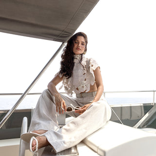 Women's lace-detailed ivory cape with soft ruffles and high neck, paired with flared trousers – romantic outfit for seaside events