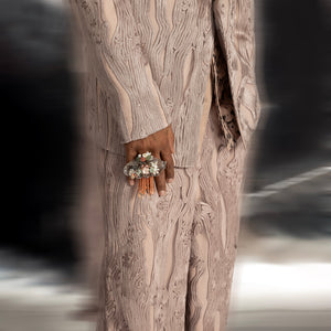 Close-up of blush yarn-couched menswear suit with intricate floral statement ring – artisanal couture detail