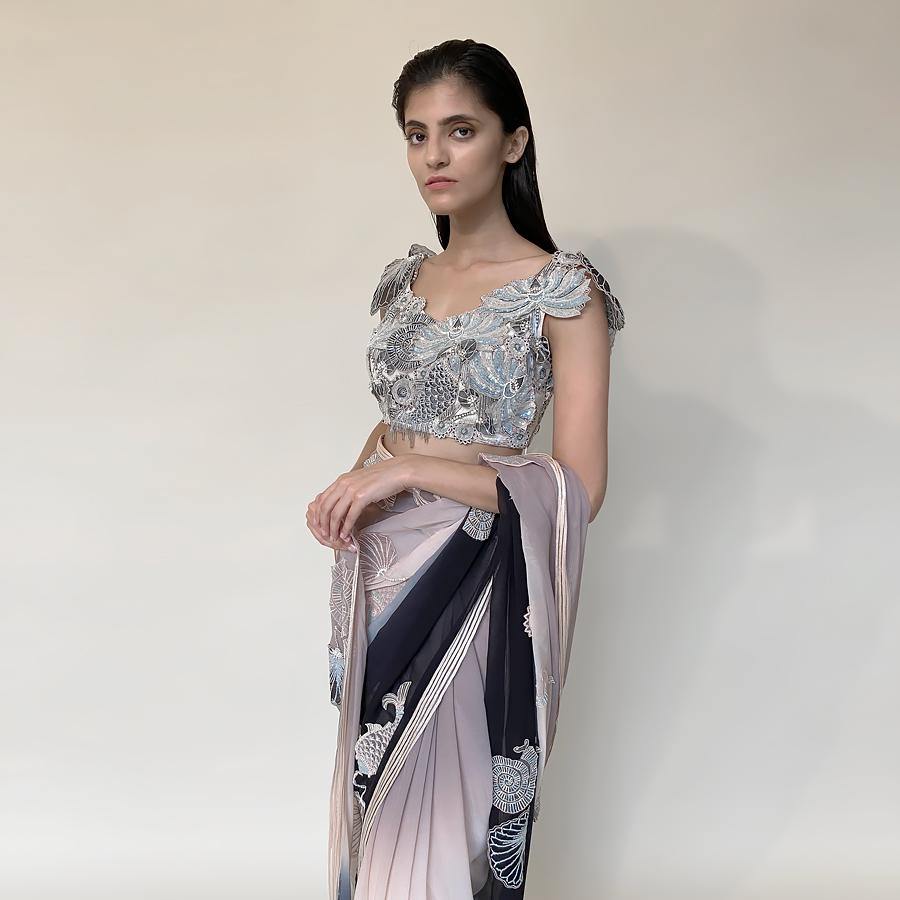 Chiffon saree ombre dyed in grey/peach/black hues. Saree is finished with contrast satin border and satin texture embellishment. Jewel neck blouse is meticulously embellished with a mix of 3D placement embroidery in thread, pearl, sequin and bugle beads. Saree possess elegance and grace as an underling feel with a dramatic play of colours and bold motifs.  Abhishek Sharma, abhishekstudio