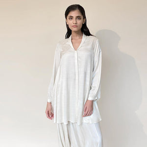 Satin circular-cut top with shawl collar and placement fine Resham and pearl embroidery teamed up draped pants. The look has an elegant and graceful vibe with a hint of style. It's a perfect pick for the day when you want to slay in style and comfort.   styling: Nude heel will complete the look along with diamond studs and ring. abhishekstudio, Abhishek Sharma 