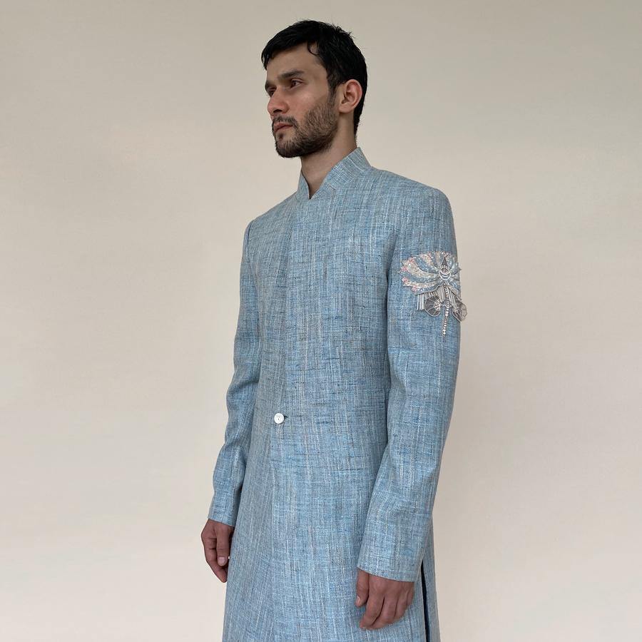 Shaped mandarin collar sherwani with single button front overlap closure. Heavy weight cotton khadi sherwani features high slits and slightly layered panels for that extra ease while sitting and or on the go. Sherwani is embellished with sequin and pearl lotus appliqué on the sleeve.  abhisheksharma , abhishekstudio