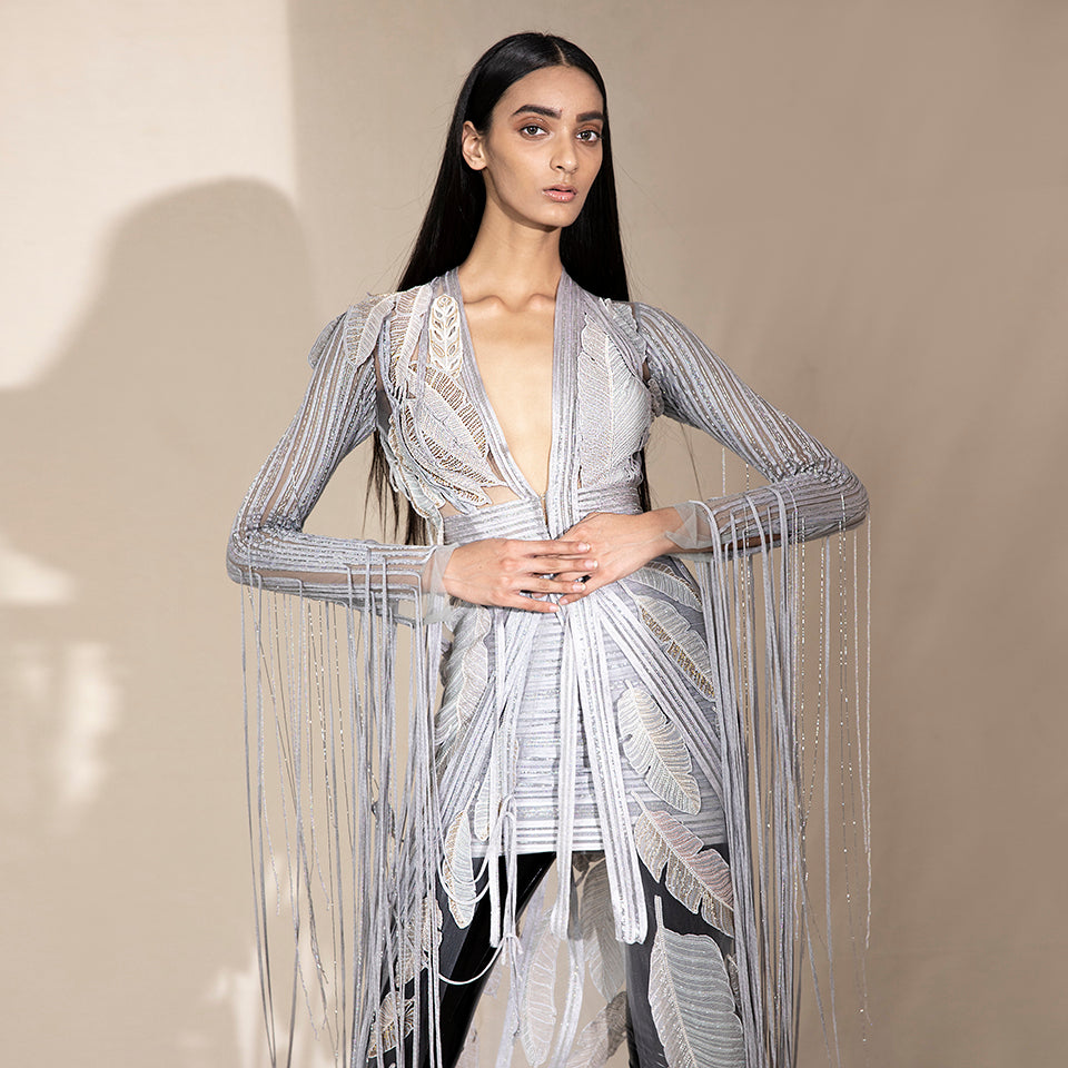 Close-up of women’s floor-length embroidered jacket with leaf motifs and beaded fringe sleeves over mini skirt – bold cocktail co-ord for parties