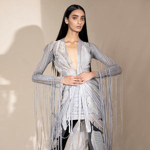 Close-up of women’s floor-length embroidered jacket with leaf motifs and beaded fringe sleeves over mini skirt – bold cocktail co-ord for parties