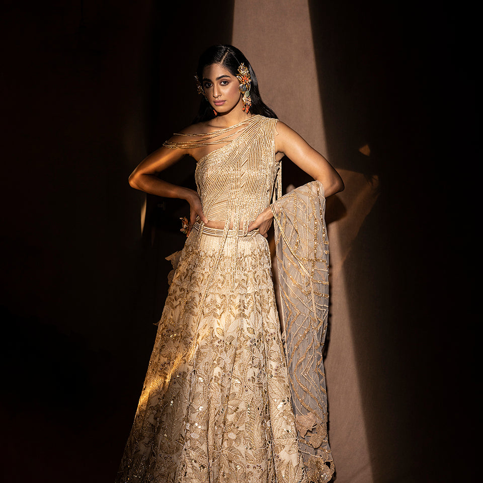 front view of Women's gold embroidered lehenga with one-shoulder drip-detail blouse and sheer dupatta – designer bridal set for sangeet or cocktail night