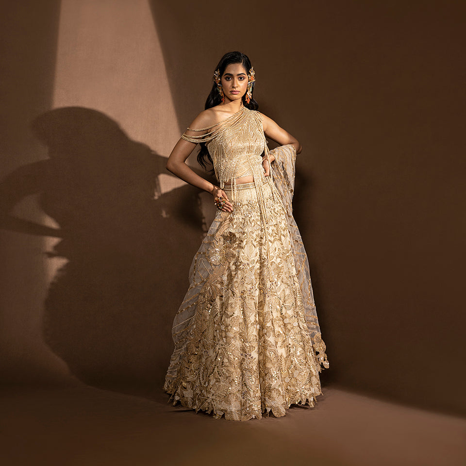 full front view of Women's gold sequin embroidered lehenga with one-shoulder layered blouse and sheer dupatta – luxury bridal co-ord for wedding or sangeet