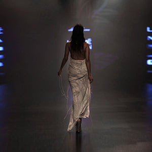 back view of Women's backless draped gown in textured ivory fabric with asymmetric hem for runway evening glamour