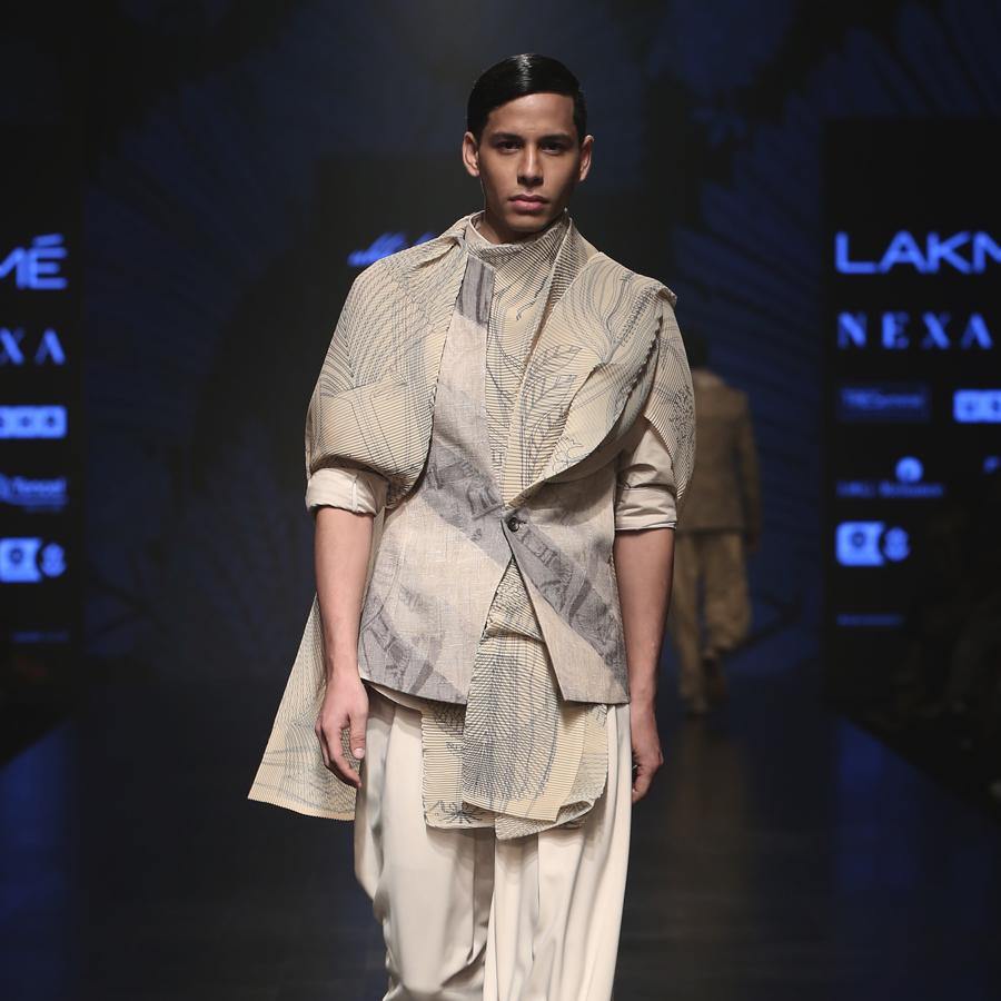 Matka silk bundi fastened with single botton closure and shaped back with double vents. Handloom silk texture is ornamented with abstract distress print in bias stripes. Structured bundi is meticulously styled over a cotton shirt with folded cuffs, then layered with a pin tuck texture forest print drape and draped baggy pants. A look that is perfect for the modern day groom who can slay. abhishek sharma, abhishekstudio