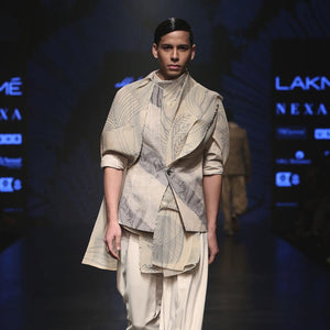 Matka silk bundi fastened with single botton closure and shaped back with double vents. Handloom silk texture is ornamented with abstract distress print in bias stripes. Structured bundi is meticulously styled over a cotton shirt with folded cuffs, then layered with a pin tuck texture forest print drape and draped baggy pants. A look that is perfect for the modern day groom who can slay. abhishek sharma, abhishekstudio